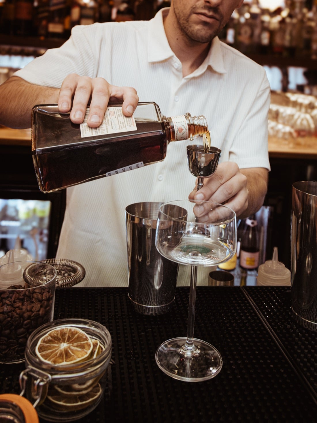 A bartender measuring a spirit into a jigger over a stemmed glass
