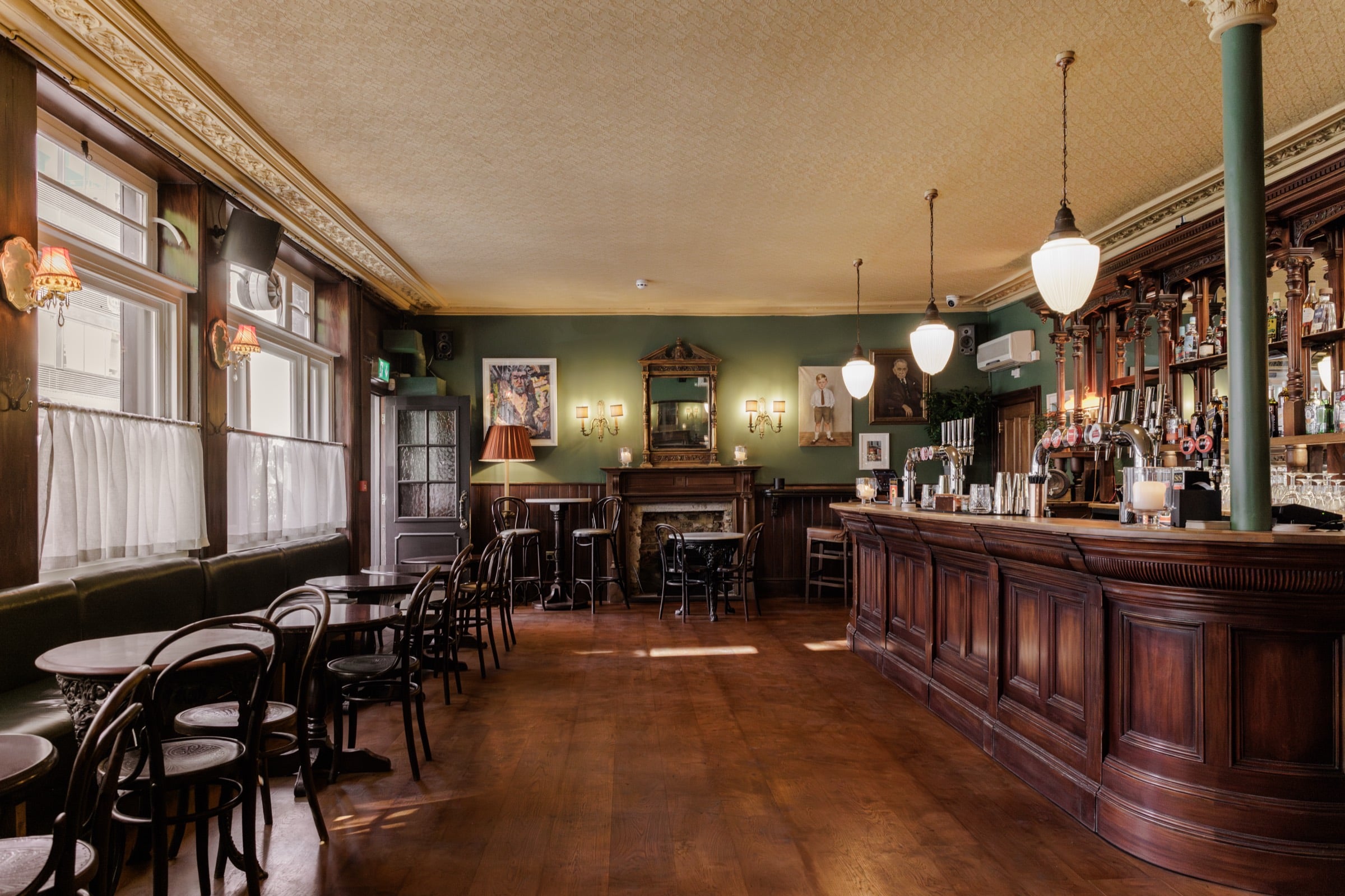 The main bar room at The Beehive, with a long mahogany bar, green walls and bentwood chairs