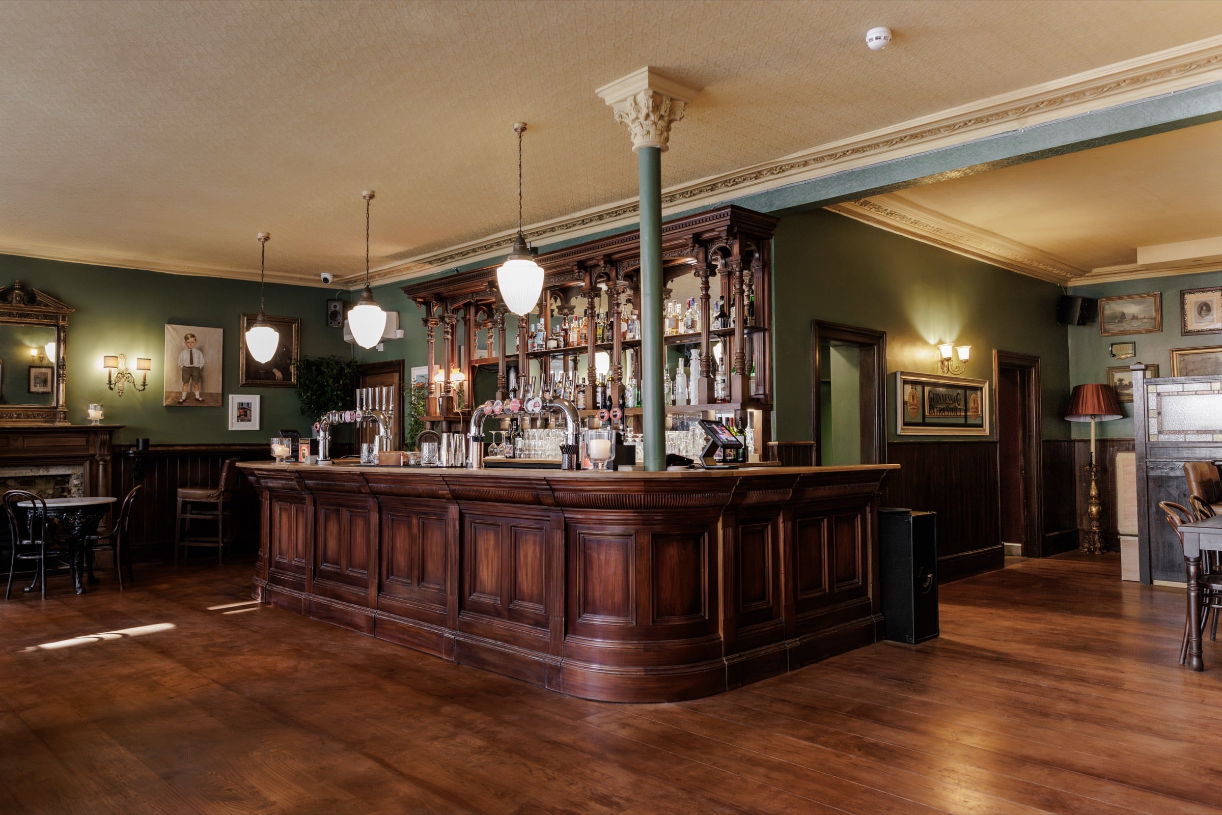 The carved mahogany island bar at The Beehive, with green walls and glass pendant lights